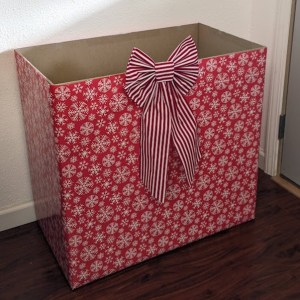 a large cardboard box wrapped in red wrapping paper with white snowflakes and decorated with a red and white striped bow