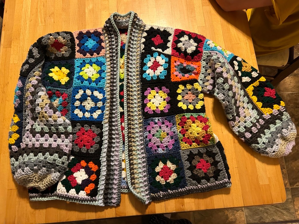 A sweater made of multi-colored granny squares laying on a table
