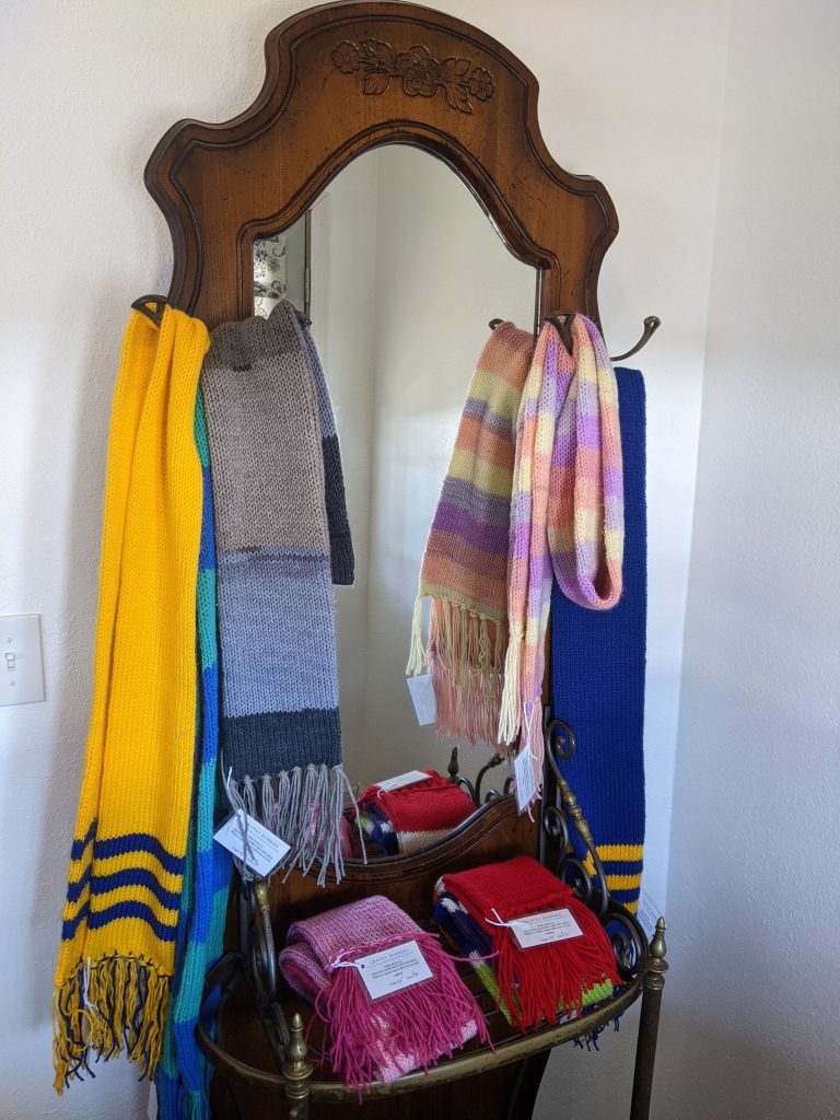 Scarves hanging on a hall tree with a mirror and scarves folded on an attached brass table.
