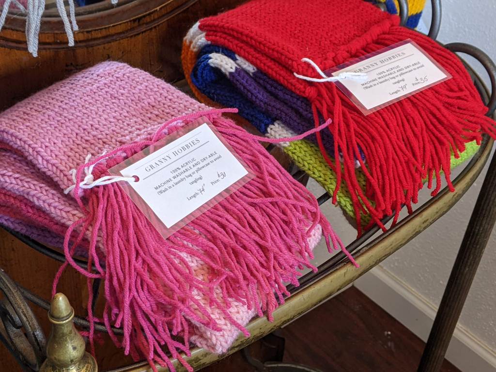 Two brightly colored tasseled scarves folded, with tags that read: Granny Hobbies, Machine Washable and Dry-Able (wash in a laundry bag or pillow case to avoid tangling).